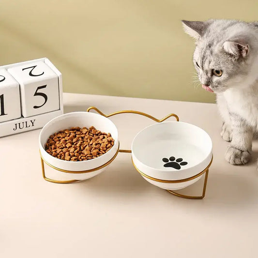 White ceramic double cat bowl with cervical protection gold metal stand and black paw print design on one bowl