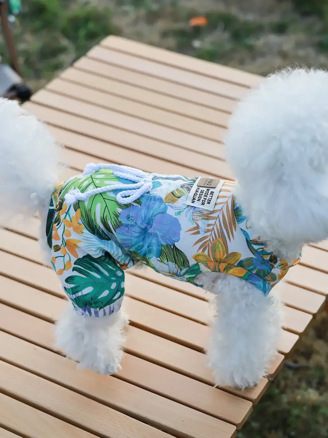 White fluffy dog wearing tropical print blue hibiscus and green leaf four legged jumpsuit for small pets