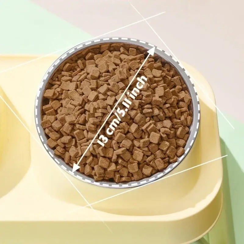 A round silver-rimmed pet food bowl filled with brown kibble in a foldable elevated dual pet feeder