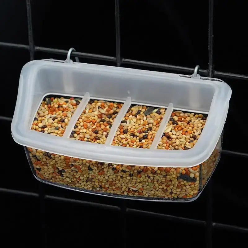 Clear plastic hanging bird and poultry feeder drinker box with four compartments filled with mixed seeds