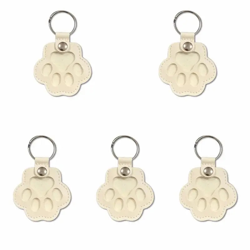Cream-colored leather pet fur memorial keepsake keychain with paw print design and silver metal ring for hair storage